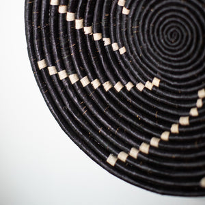 JustOne's black wall basket with tan stripes spiralling out, handwoven in Uganda