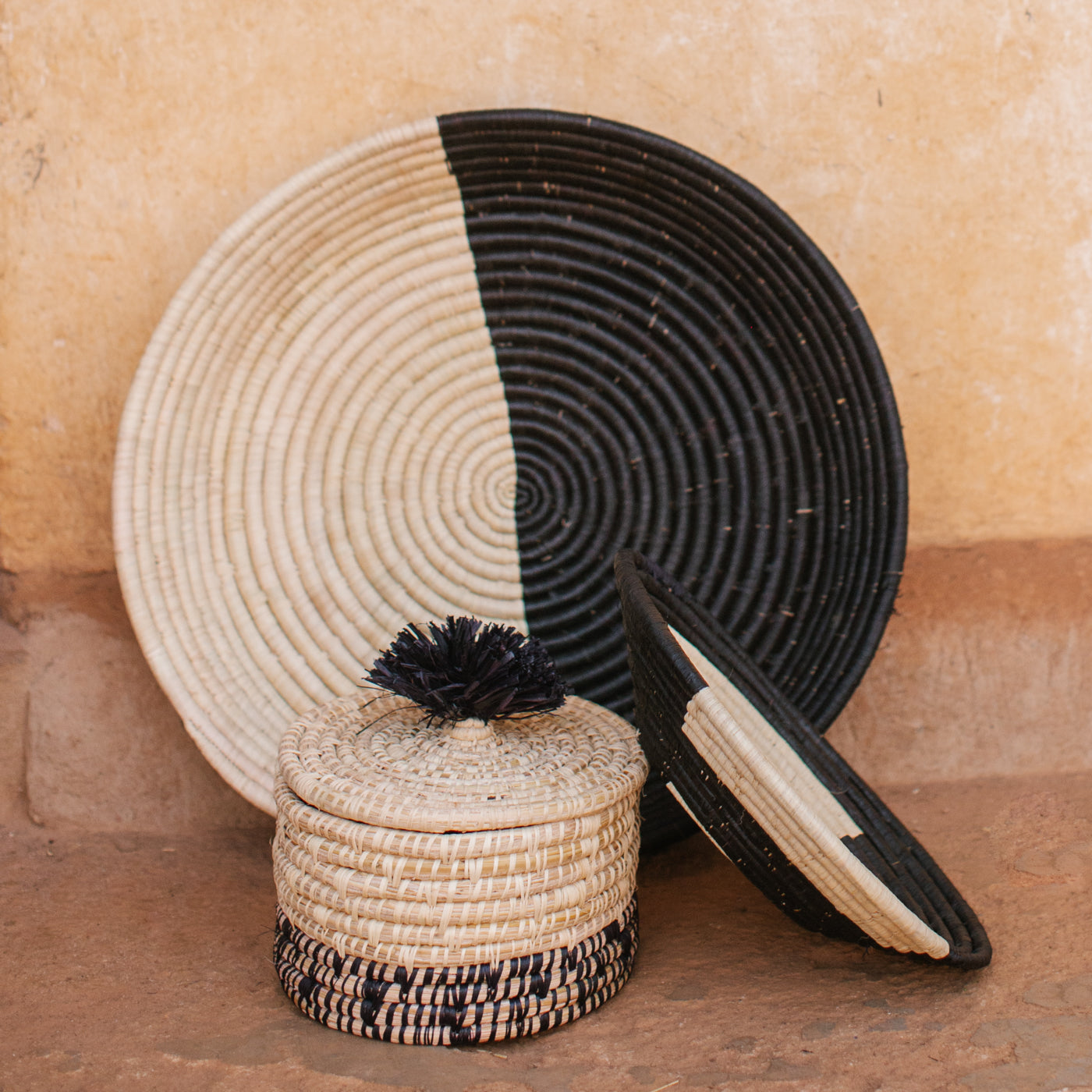 JustOne's natural basket with black details on bottom and lid with a black pompom handle, handcrafted in Uganda