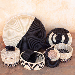 A collection of JustOne's baskets with a feature on the small tan basket with a black and natural border, handwoven in Uganda