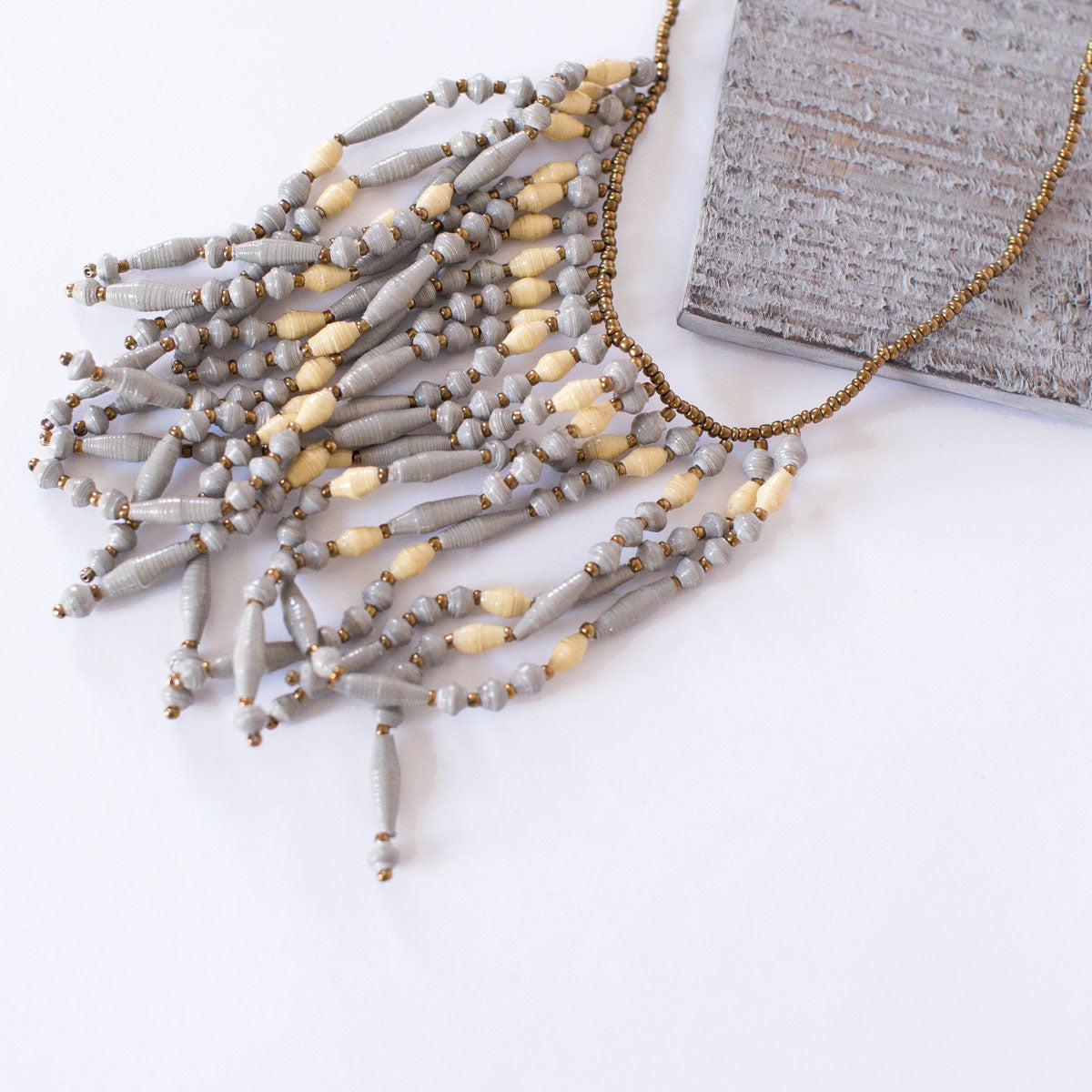 JustOne's necklace with several dangling strings of paper beads in grey and tan colours, handcrafted in Uganda