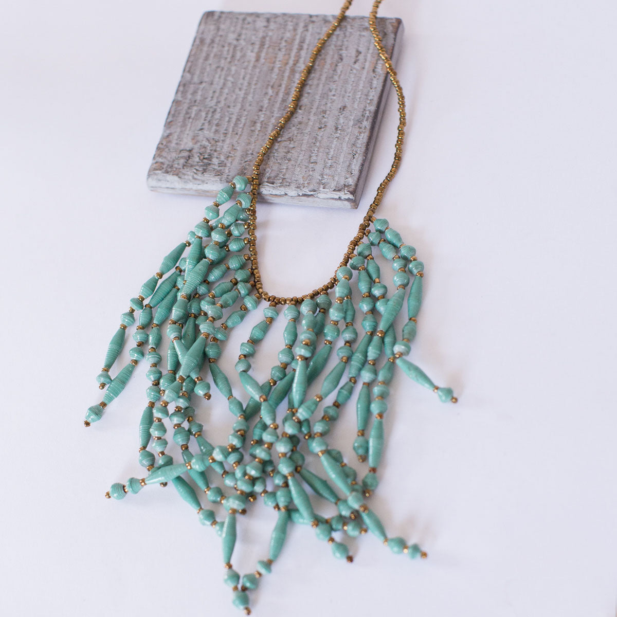 JustOne's necklace with several dangling strings of paper beads in teal, handcrafted in Uganda