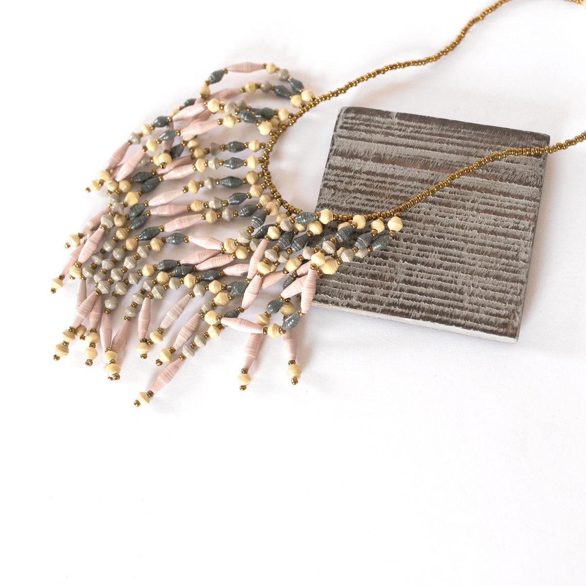 JustOne's necklace with several dangling strings of paper beads in grey, pink, and tan colours, handcrafted in Uganda