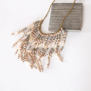 JustOne's necklace with several dangling strings of paper beads in muted grey, pink, and tan colours, handcrafted in Uganda
