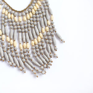 JustOne's necklace with several dangling strings of paper beads in grey and tan colours, handcrafted in Uganda