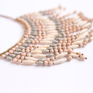 JustOne's necklace with several dangling strings of paper beads in muted grey, pink, and tan colours, handcrafted in Uganda