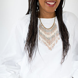 JustOne's necklace with several dangling strings of paper beads in muted grey, pink, and tan colours, handcrafted in Uganda
