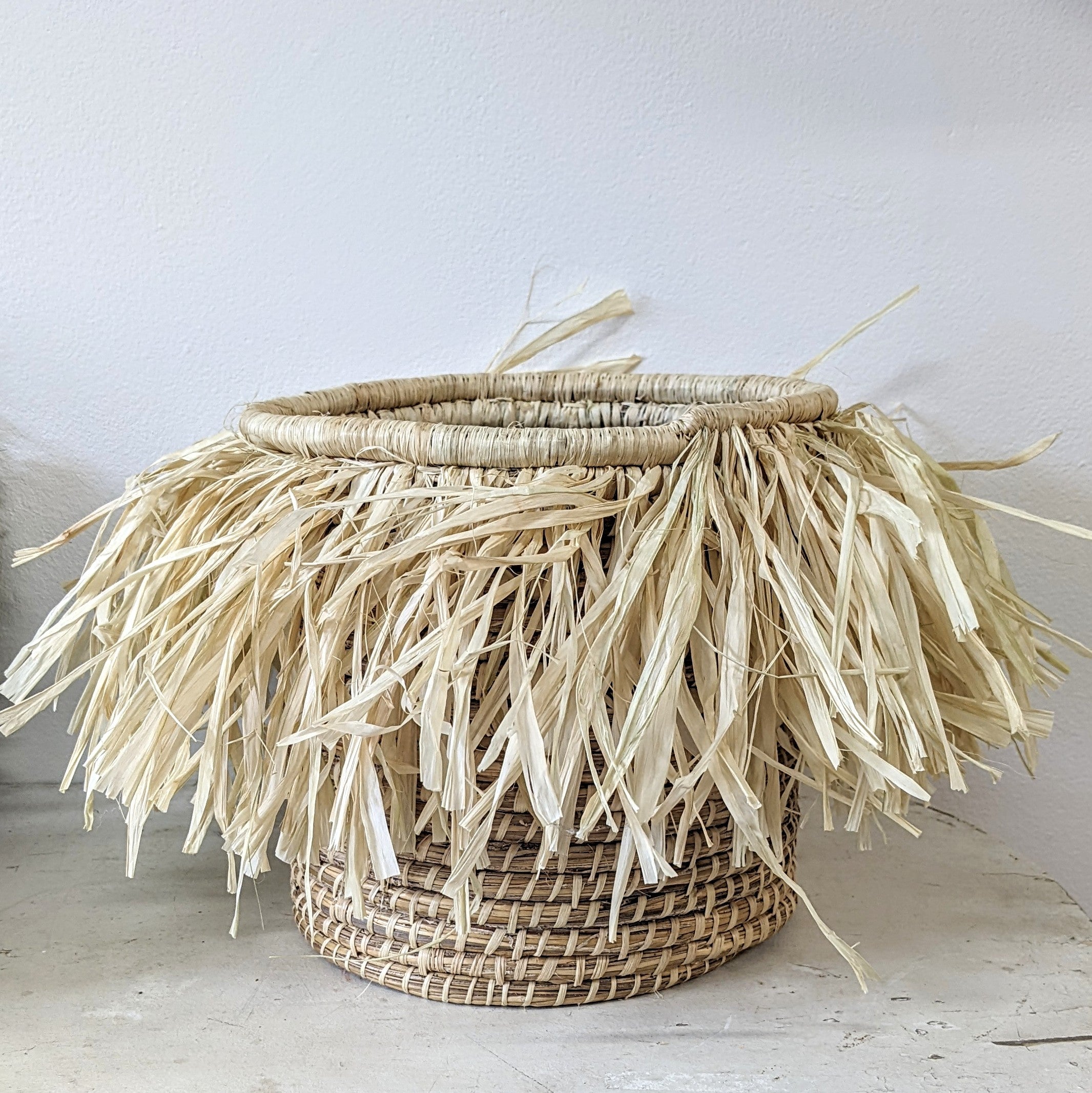JustOne's medium tan basket with tan fringe surrounding the basket, handwoven in Uganda
