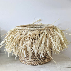 JustOne's medium tan basket with tan fringe surrounding the basket, handwoven in Uganda