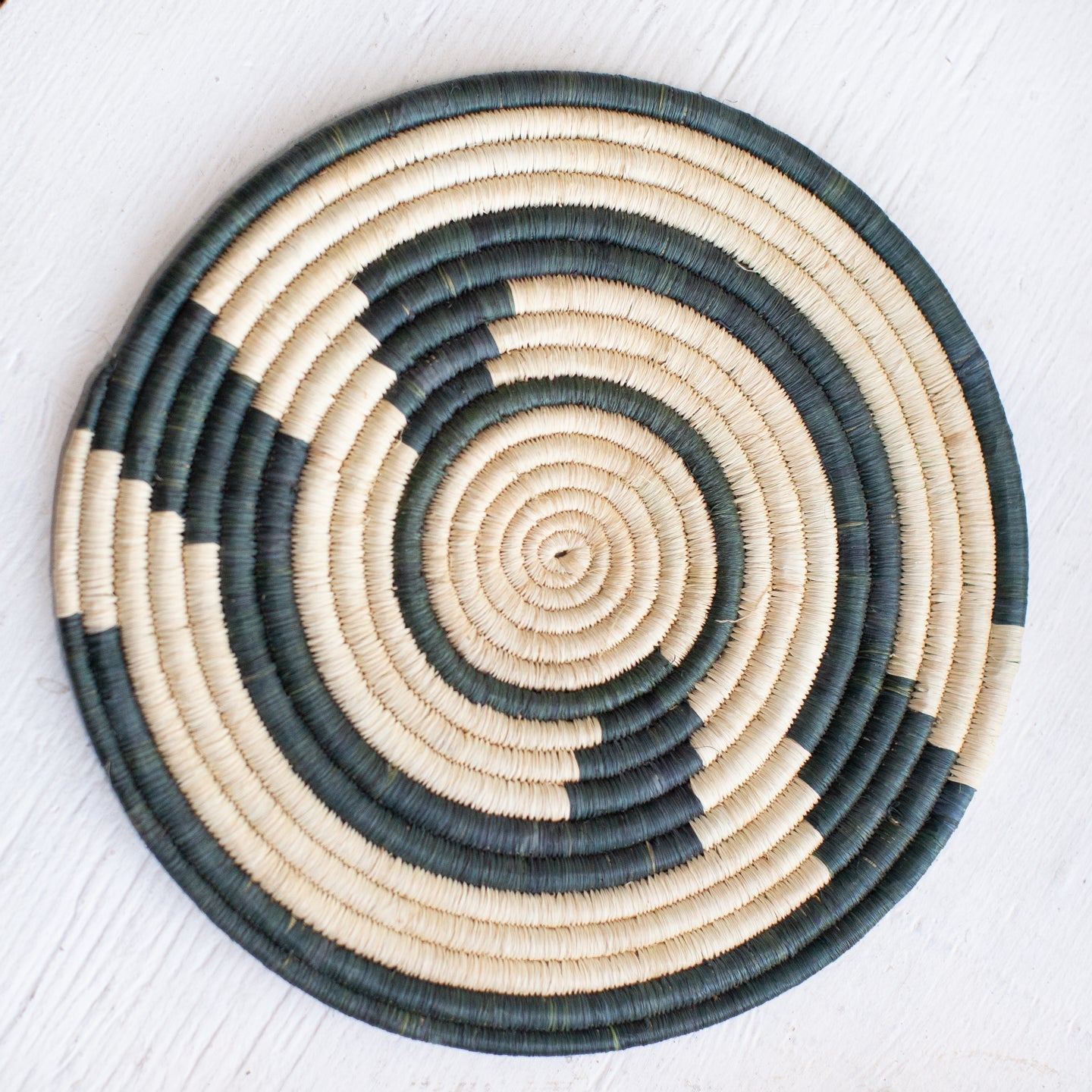 JustOne's large flat basket with tan and dark green twisting around the circle, handwoven in Uganda