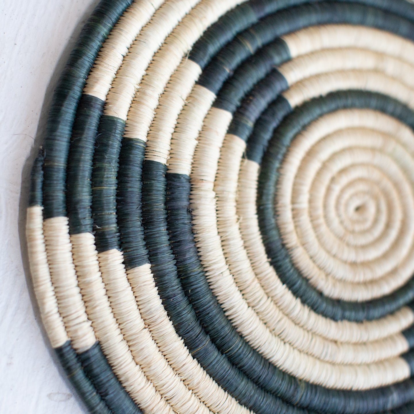 JustOne's large flat basket with tan and dark green twisting around the circle, handwoven in Uganda