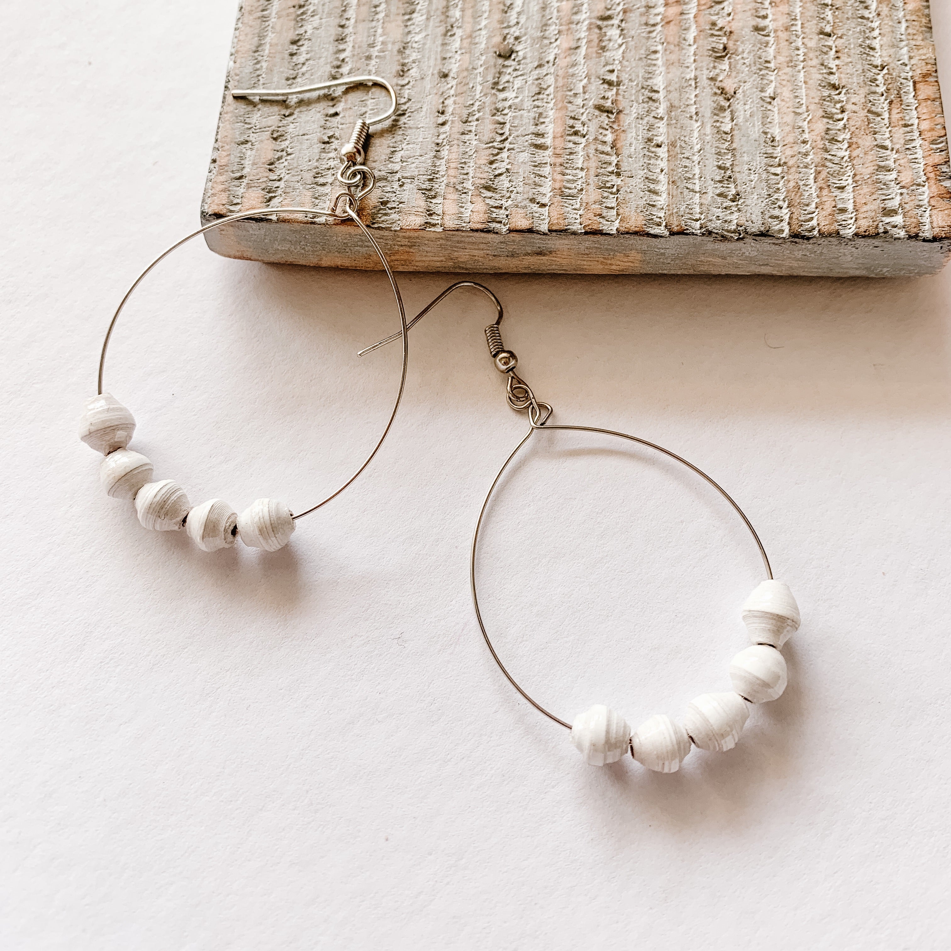 JustOne's silver hoop earrings with five white paper beads on the bottom of the hoop, handcrafted in Uganda